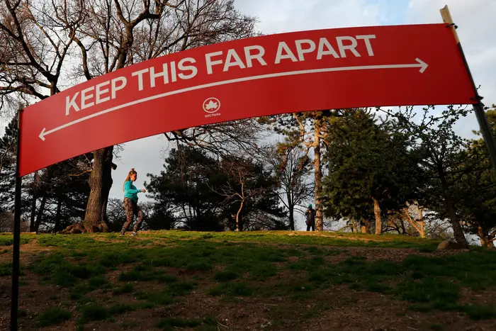 Woman jogs in Brooklyn's Fort Greeene park, beneath a sign demonstrating the distance people should keep from each other during the coronavirus outbreak in New York.